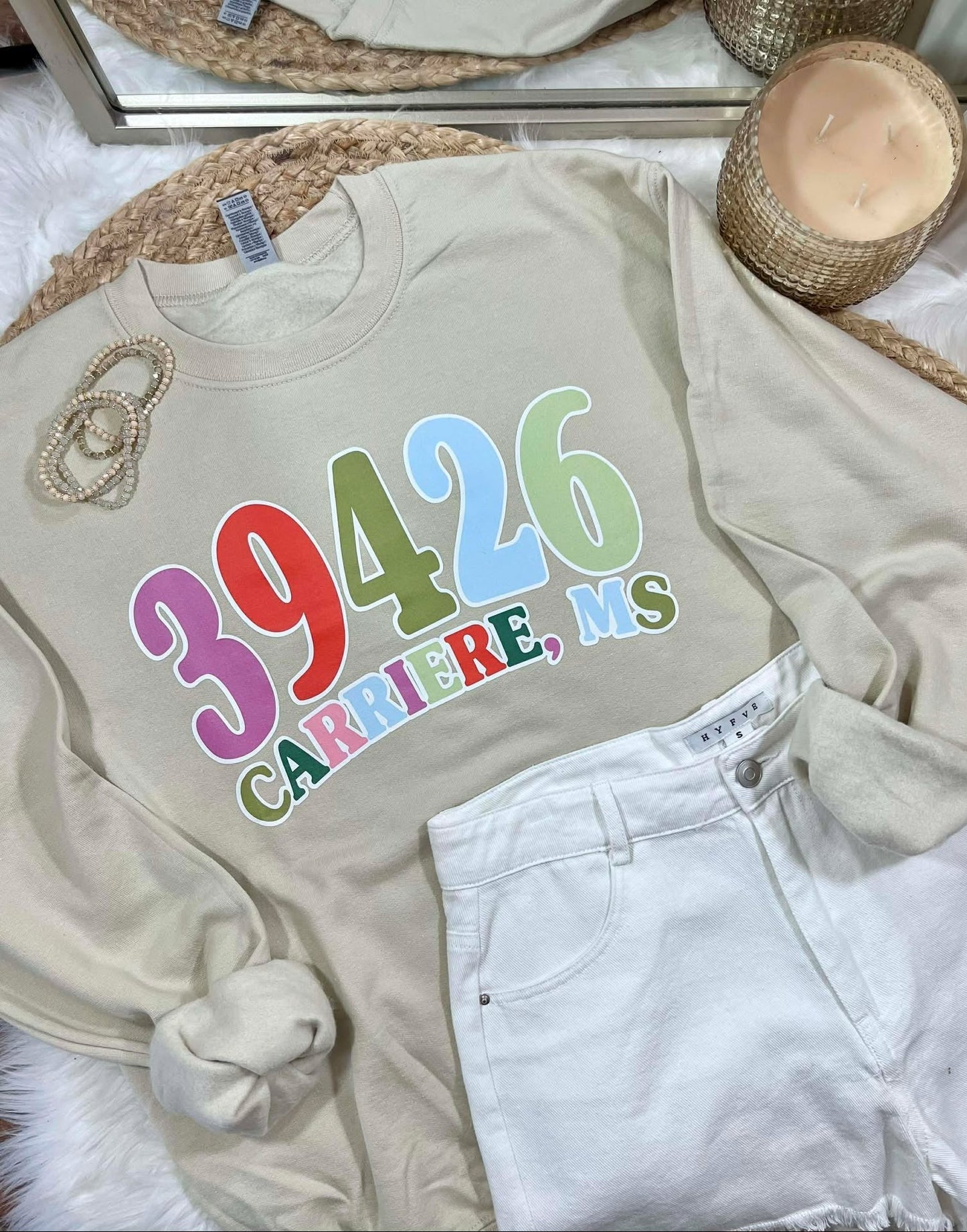Beige sweatshirt with colorful zipcode text on a bed