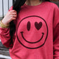 Person wearing a red sweatshirt with a smiley face design outdoors.