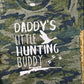 A vintage camouflage colored t-shirt with the text 'Daddy's Little Hunting Buddy' printed on the front.