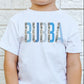 A child wearing a white short-sleeved t-shirt with the text 'BUBBA' printed in blue camo colorblock style on the front.