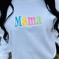 A white sweatshirt with the word 'mama' embroidered in multicolored letters on the front.
