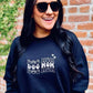 A woman smiling and wearing a black sweatshirt with the text 'Dog Mom' and a small wave symbol embroidered on it.