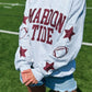 Person wearing a gray sweatshirt with 'Marion Tide' text and sports graphics on a grassy field.