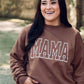A person wearing an embroidered sweatshirt with the word 'mama' on the front, paired with denim shorts.