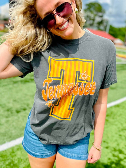 Woman wearing a gray t-shirt with a large yellow number '1' and 'Tennessee' text, standing on a grassy field.