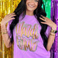A person wearing a neon violet t-shirt with the text 'Mardi Gras' printed on it, surrounded by colorful confetti background.