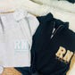 Two hooded jackets, one black and one gray, laid out on a white surface with 'RN' embroidered in gold on the front. Both jackets have a crew neck and a 1/4 zip design.