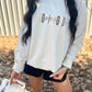 A person wearing a light-colored, embroidered sweatshirt with the text 'GOD IS GOOD' on the front, standing outdoors.