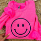 A neon pink sweatshirt with a black smiley face embroidered on the front, displayed on a furry surface.