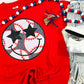 A red graphic tee with a baseball and stars design, accompanied by blue and white beaded necklaces and a black hair tie.