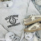 A gray embroidered sweatshirt with 'Silly Goose University' text on the front, paired with white sneakers with embellishments on the sole.