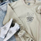 A sand-colored embroidered sweatshirt with a graphic of a bunny wearing glasses, paired with white sneakers and blue jeans.