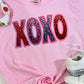 Pink sweatshirt with 'XOXO' in colorful letters on a white surface.