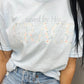 A person wearing a light blue t-shirt with the text 'saved by His grace' and a floral design.