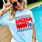 A person sitting by a poolside wearing a light blue graphic t-shirt with the text 'AMERICAN HONEY' in a patriotic design.