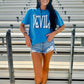 Person wearing a blue 'DEVIL' t-shirt in bleacher seating area