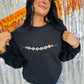 A person wearing a black sweatshirt with 'Spooky Friendship Bracelet' embroidered on the front, posing against a glittery orange background.
