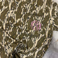 Camouflage-patterned shirt with pink monogram on a textured surface