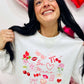 Woman wearing a white sweatshirt with Valentine's Day designs surrounded by heart-shaped decorations.