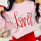Person wearing a pink sweatshirt with 'Lover' written in red, standing against a white background.