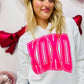 A person wearing a white V-neck sweatshirt with 'XOXO' printed in neon pink vinyl on the front.