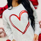 Woman wearing a gray sweatshirt with a red heart design, standing against a white background with red ribbons.
