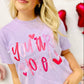 Woman wearing a purple t-shirt with 'You are love' text and hearts, surrounded by red heart-shaped props.