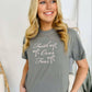 A woman smiling and wearing a gray t-shirt with 'Faith & Fear' embroidered on the front.