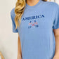 A woman wearing a blue t-shirt with 'America 1776' and a flag-themed design embroidered on the front.