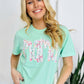 A woman smiling and wearing a green t-shirt with a multicolored floral farm DTF print.