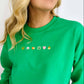 A woman wearing a green embroidered sweatshirt with decorative elements on the front.