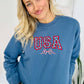 A woman wearing a blue sweatshirt with 'USA' and a star and bow embroidered on the front.