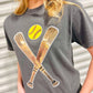 A female model wearing a gray t-shirt with a sequin patch on the front showing two softball bats and a yellow softball.