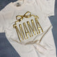 An ivory colored t-shirt with the word 'MAMA' printed in gold metallic vinyl in a bow shape.