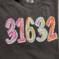 A folded black t-shirt with the zip code '31632' painted in various colors on the front.