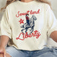 A person wearing an ivory colored graphic tee with the text 'Sweet land Liberty' and a cowboy illustration.
