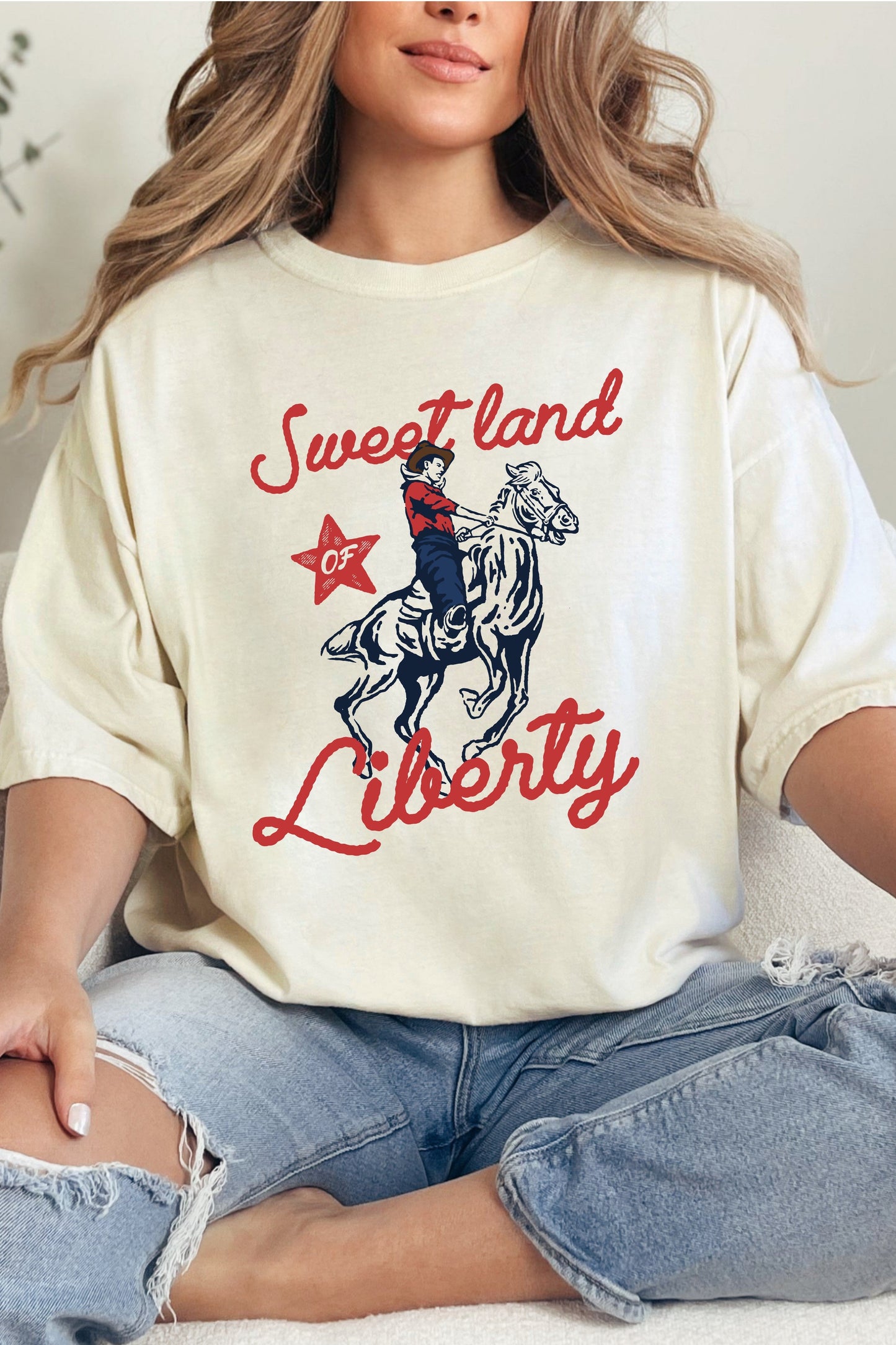A person wearing an ivory colored graphic tee with the text 'Sweet land Liberty' and a cowboy illustration.
