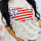 A graphic tee with a patriotic theme featuring an outline of the United States in red and blue colors with a bow on it, against a natural heather star pattern.