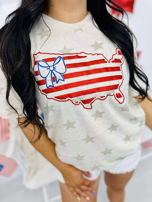 A graphic tee with a patriotic theme featuring an outline of the United States in red and blue colors with a bow on it, against a natural heather star pattern.