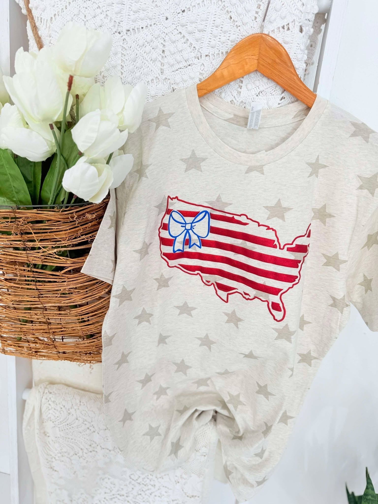 Baby onesie with USA design and bow on stars background next to white tulips in a basket.