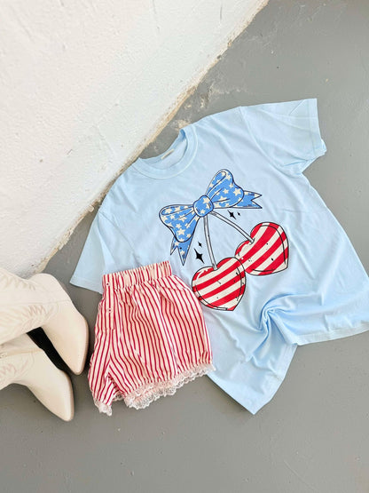 Light blue t-shirt with red and white heart cherry design and red shorts on a light gray surface.