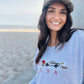 Woman wearing a light blue sweatshirt with an eagle, cowboy boots, truck and usa flag graphic design, sitting on a beach.