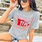 Person wearing a gray t-shirt with 'Gameday Tide' text and logo, sitting outdoors.