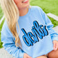 Person wearing a light blue sweatshirt with 'devils' printed on it, sitting on a grassy field.