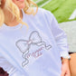 Person wearing a white sweatshirt with a bow design and 'Maroon 5' text, sitting outdoors.