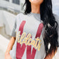 Woman wearing a gray t-shirt with 'Wildcats' printed on it, standing outdoors.