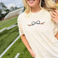Woman wearing a cream t-shirt with a football bow design on a sports field