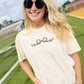 Woman wearing a cream t-shirt with a bow football design on a sports field