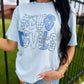 Person wearing a light blue t-shirt with 'Blue Devils' text and plaid design outdoors.