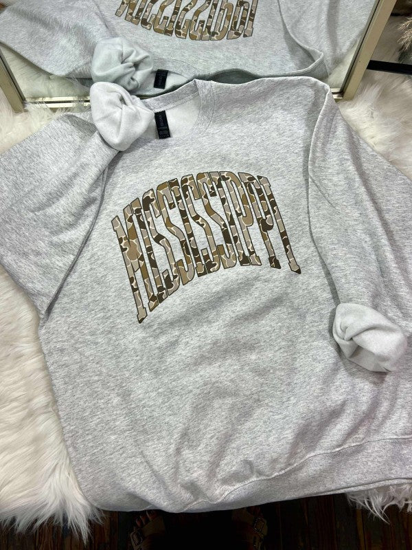 Gray sweatshirt with decorative duck camo text MISSISSIPPI curved arched on a fluffy surface